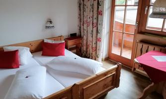 A cozy bedroom with a double bed and red pillows. Large windows let in plenty of light and provide access to a balcony.