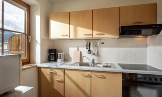 A modern kitchen with wooden cabinets and a window that lets in plenty of light. The kitchen equipment includes a stove, a refrigerator, and a coffee maker.