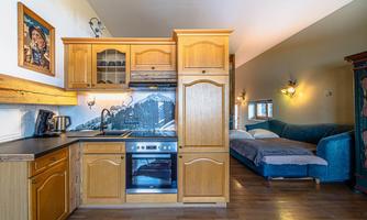 A modern kitchen with wooden cabinets and a stove. In the background, a cozy sofa and a bed are visible.