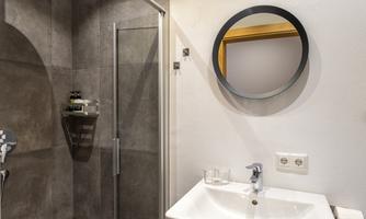 A modern bathroom with a shower and a sink. On the wall, there is a round mirror and the tiles are in neutral tones.