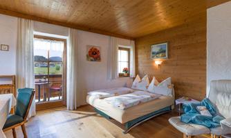 A cozy room with wooden decor and a double bed. A beautiful view of the outdoors is visible through the windows.