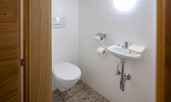 A simple bathroom with a toilet and a small sink. There are towels and toilet paper available.