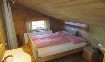 A cozy bedroom with wood decor. The room has a large bed with red cushions and a window with a lovely view.