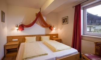 A cozy bedroom with two single beds and wooden furniture. The windows provide daylight and the walls are in soft colors.