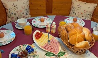 A lavish breakfast table with rolls, cold cuts, cheese, and fresh fruit. There are also coffee, tea, and juices in a cozy atmosphere.