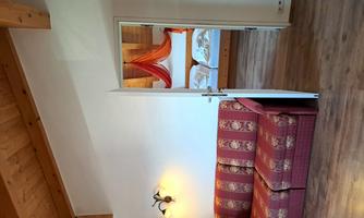 A cozy room with a red sofa and a bedroom in the background. The bed is adorned with decorative curtains in orange.