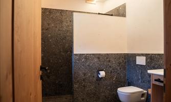 A modern bathroom with a shower, toilet, and elegant stone walls. The atmosphere is simple and stylish.