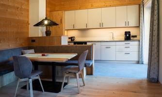 A modern kitchen with wood walls and a dining area. The room is bright and inviting, with a table and chairs.