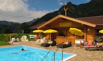 An inviting outdoor pool with sun loungers and yellow umbrellas. In the background, mountains and a wooden house can be seen.
