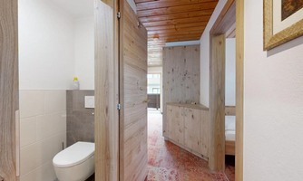 A modern hallway with wooden details and a bathroom on the left side. The space is brightly and invitingly designed.