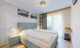 A cozy bedroom with a double bed and bright walls. Large windows provide plenty of daylight and a pleasant atmosphere.