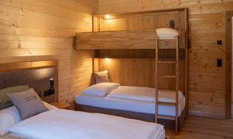 A cozy room with wooden paneling. There is a loft bed and a single bed, both with white duvets.