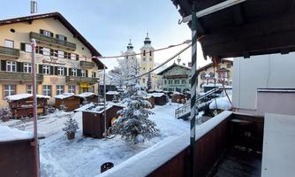 A winter landscape with snow-covered cottages and a festively decorated tree. In the background, historical buildings and towers can be seen.