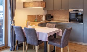 A modern kitchen with a dining area. A table with chairs and a large window front create a bright atmosphere.