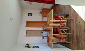 A cozy dining area with a wooden table and chairs. The walls are light, and there is a red curtain as well as some decorations.