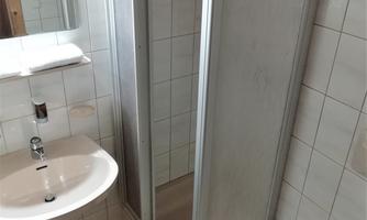 A simple bathroom with a shower, sink, and mirror. The walls are tiled, and a towel is ready.