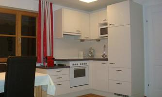 A modern kitchen with white cabinets and a contemporary cooking area. There is a table with chairs and large windows that provide plenty of light.