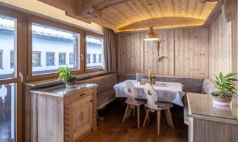 A cozy dining area made of wood with a round table and bright chairs. Large windows provide plenty of daylight and a pleasant atmosphere.