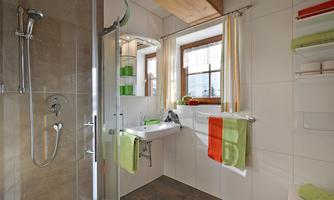 A modern bathroom with a shower and a sink. There are colored towels and natural light sources from windows.