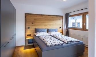 A modern bedroom with a large bed and wooden paneling. Large windows provide plenty of daylight.