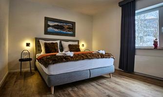 A cozy bedroom with a large bed and modern design.  
Large windows let in plenty of daylight and offer a view outside.