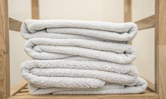 Stacked, clean towels on a wooden shelf. The towels are light gray and neatly folded.