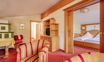 A cozy room with red-striped armchairs and a dining table. In the background, there is a bedroom with a double bed.