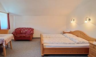 A cozy room with two beds and a red sofa. There is a table and a bright, inviting atmosphere.