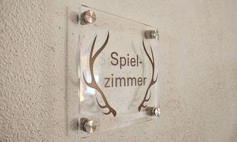 A modern sign with the inscription "Playroom" and stylized antlers. It is mounted on a light wall.