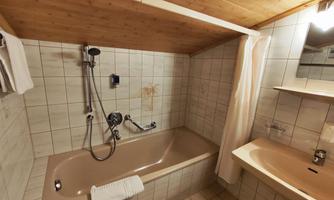 A bathroom with a bathtub and a sink. The walls are tiled and there are wooden panelings on the ceiling.