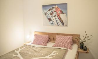 A cozy bedroom with a double bed, checkered pillows, and a wall decoration featuring mountain motifs. The room has a bright, inviting atmosphere.