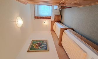 A simple bedroom with two single beds and a large window. An artwork hangs on the wall, and the room has wooden paneling.
