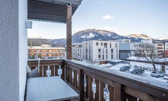 A balcony with a table and a view of snow-covered mountains. The sky is clear and there are some clouds visible.