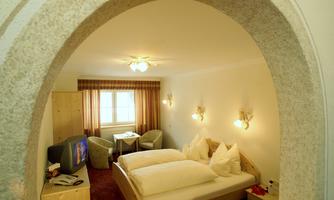 A cozy hotel room with a large bed and two comfortable chairs. There is a television and a table, and the light creates a warm atmosphere.