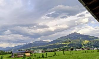 A picturesque landscape with green meadows and gentle hills. In the background, majestic mountains rise under a cloudy sky.