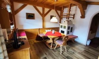 A cozy dining area in a wooden house with a round table and chairs. On the wall, there is a television and a decorative lamp above the table.