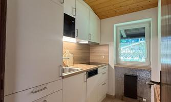 A modern kitchen with white cabinets and a bright wood ceiling. The window offers a view outside and provides natural light.