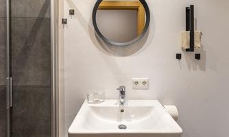A modern bathroom with a sink and a round mirror. In the background, a shower can be seen.