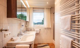 A modern bathroom with a large sink and a window that offers a view of nature. White towels and a warm color tone create an inviting atmosphere.