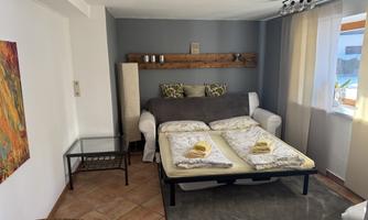 A cozy room with a sofa bed and a small table. Soft colors and plenty of light create an inviting atmosphere.