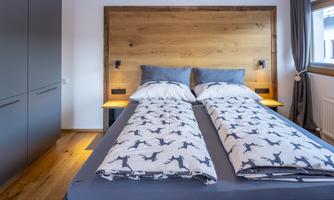 A modern bedroom with a double bed and a wooden headboard. The walls are painted in neutral colors and the floor is made of wood.
