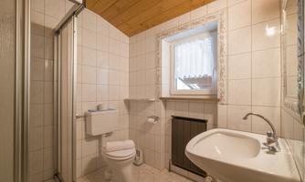 A modern bathroom with a shower, toilet, and sink. Bright tiles and a window create a welcoming atmosphere.