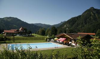 A pool in front of picturesque mountains and a green landscape. Sun umbrellas and loungers invite relaxation.