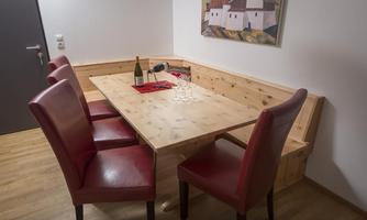 A dining area with a wooden table and red chairs. On the table is a bottle of wine and glasses.