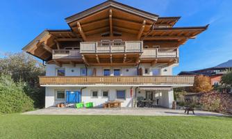 A beautiful chalet with wooden cladding and several balconies. The large garden and clear sky give the surroundings an inviting atmosphere.