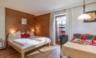 A cozy bedroom with a double bed and wood paneling. On the table, there is a tablecloth and some snacks ready.