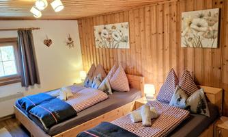 A cozy bedroom with two beds and wooden paneling. The walls are decorated with beautiful pictures and warm light.
