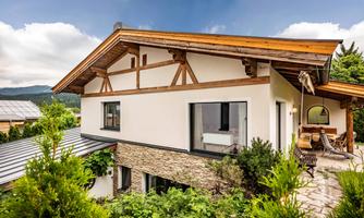 A modern house with wooden and stone elements in a green environment. The garden is beautifully designed and invites you to relax.