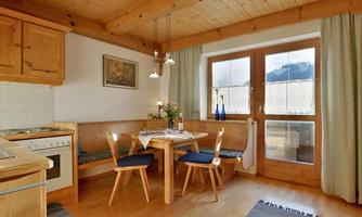 A cozy kitchen with wood decor and a table. Large windows offer a view of nature.