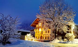 A beautiful, snow-covered Tyrolean inn under a clear night sky. The snow sparkles picturesque in the light of the nearby illumination.